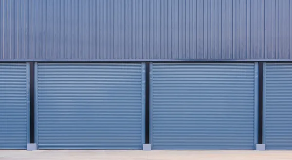Fachada de una bodega con dos puertas industriales enrollables de metal azulado, instaladas sobre un muro de lámina.