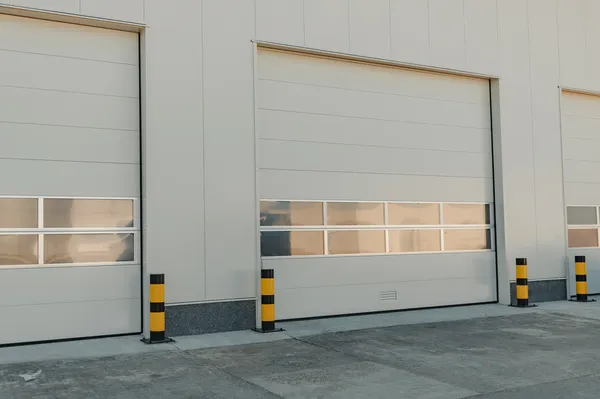 Primer plano de puertas industriales seccionales de color blanco, con ventanas y protección en un almacen industrial.