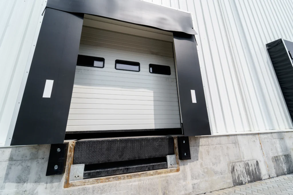 Vista en ángulo de unos sellos de anden negros instalados en el muelle de carga de una nave con fachada blanca.
