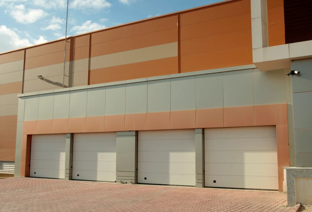 Una fachada de nave industrial moderna con cuatro accesos de puerta de sellado rápido de color blanca.