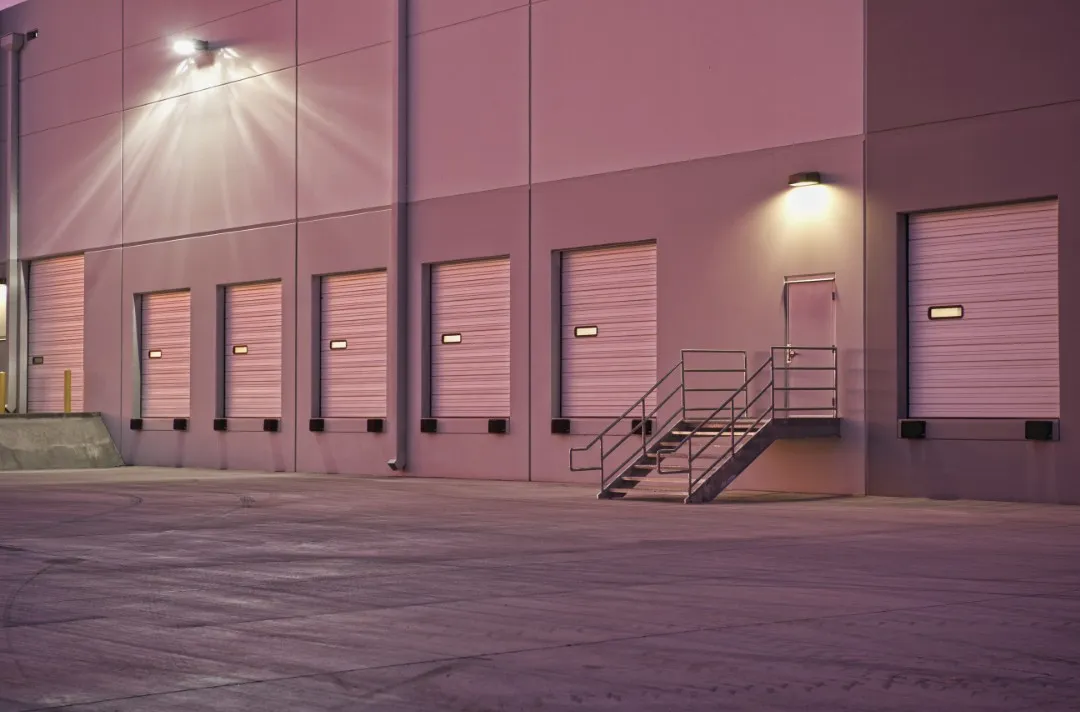 Fotografía nocturna de la fachada de una nave industrial con múltiples accesos equipados con puertas rápidas e industriales en los muelles de carga.