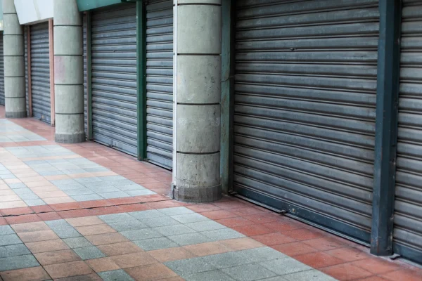 Un pasillo de centro comercial con las tiendas cerradas, cada una protegida por su respectiva cortina enrollable cerrada