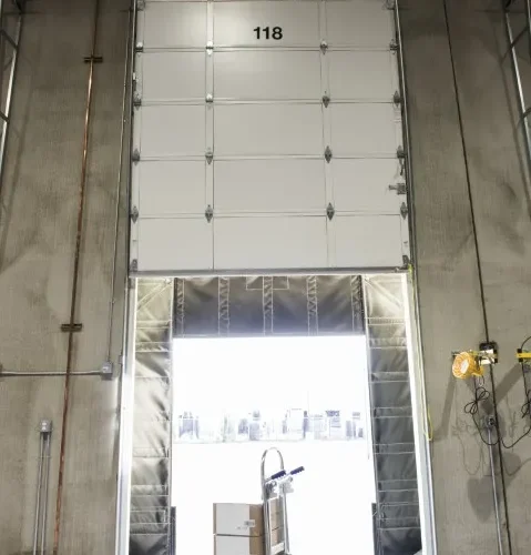 Fotografía de una puerta seccional industrial articulada en un muelle de carga, utilizada para complementar el uso de puertas rápidas en almacenes.